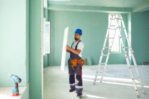 Drywall Installation being done by a worker and his ladder